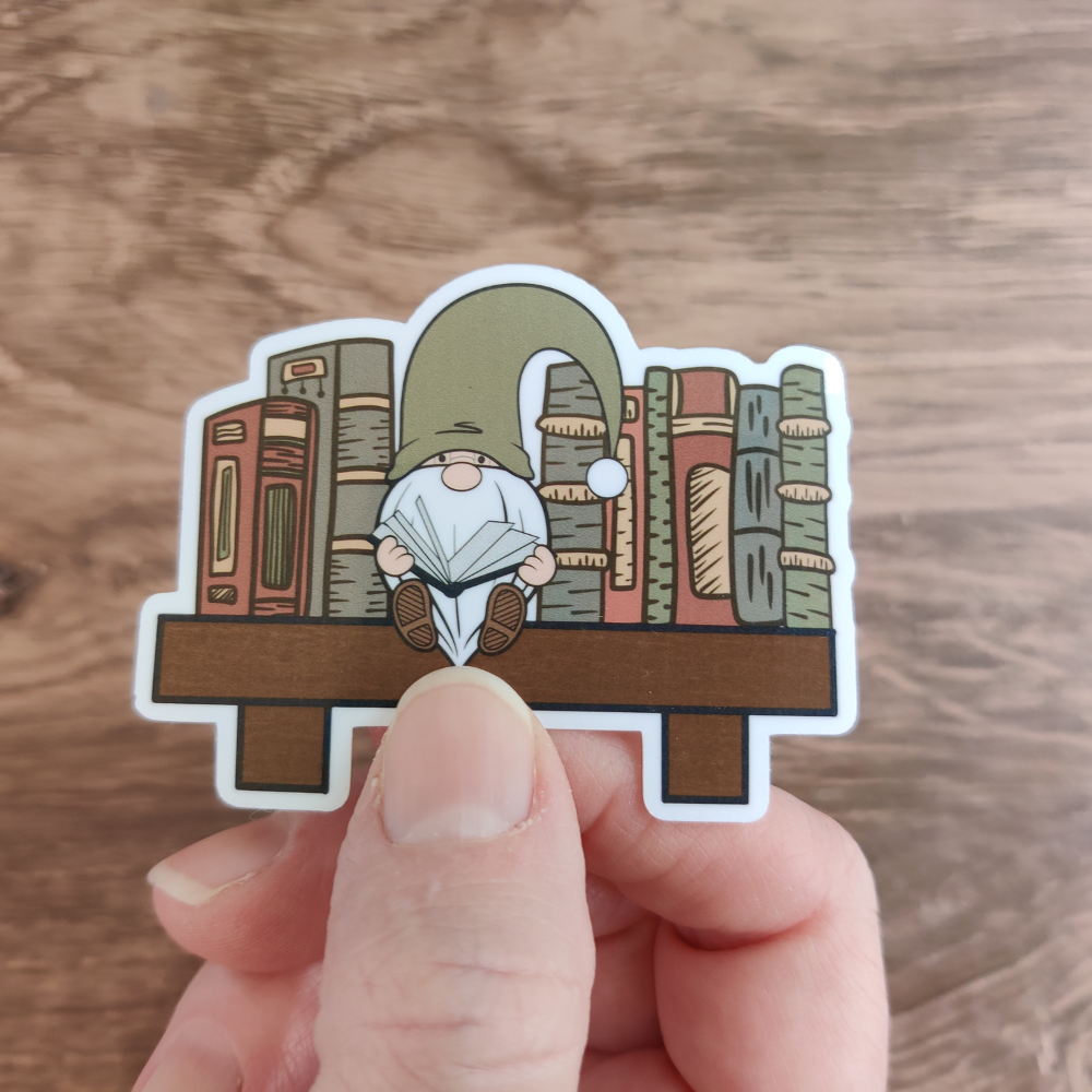 A hand holding a reading gnome sticker with a clear laminate