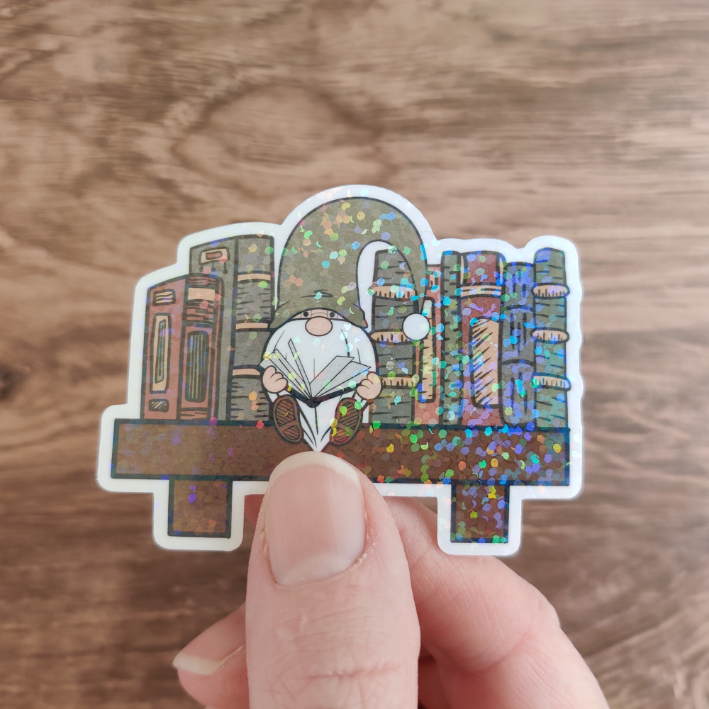 A hand holding a reading gnome sticker with a sparkle laminate.