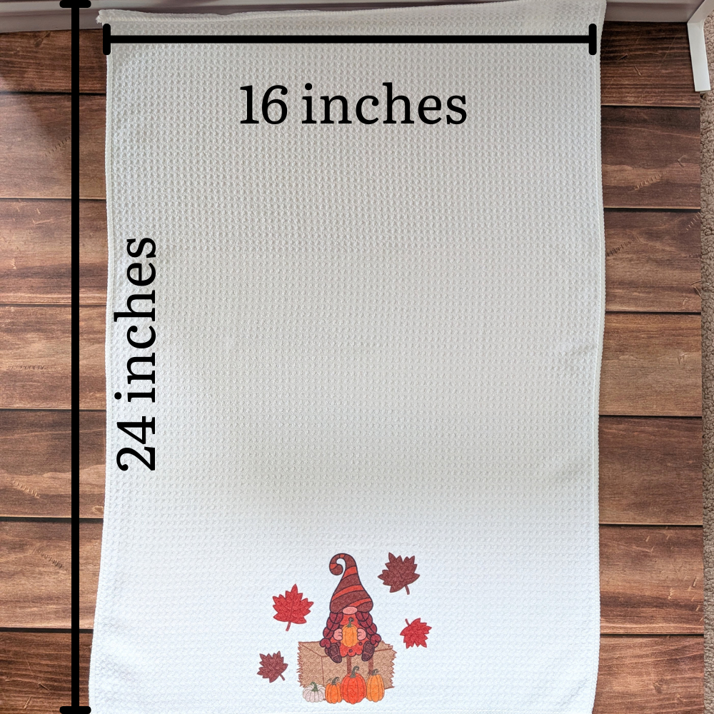 A white waffle towel with a girl fall gnome on the bottom of the towel. The image shows the size of the towel as 16 inches wide by 24 inches long when opened.