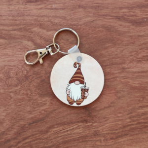 A keychain featuring a gnome wearing a brown striped hat and holding an iced coffee. The keychain is silver with a lobster claw attached.