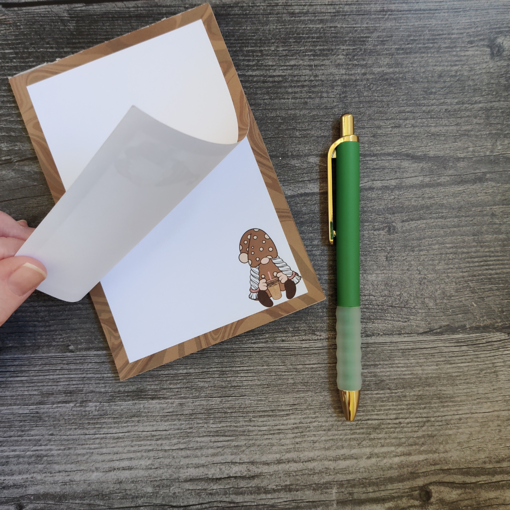 A hand flips the pages of the brown iced coffee gnome notepad.