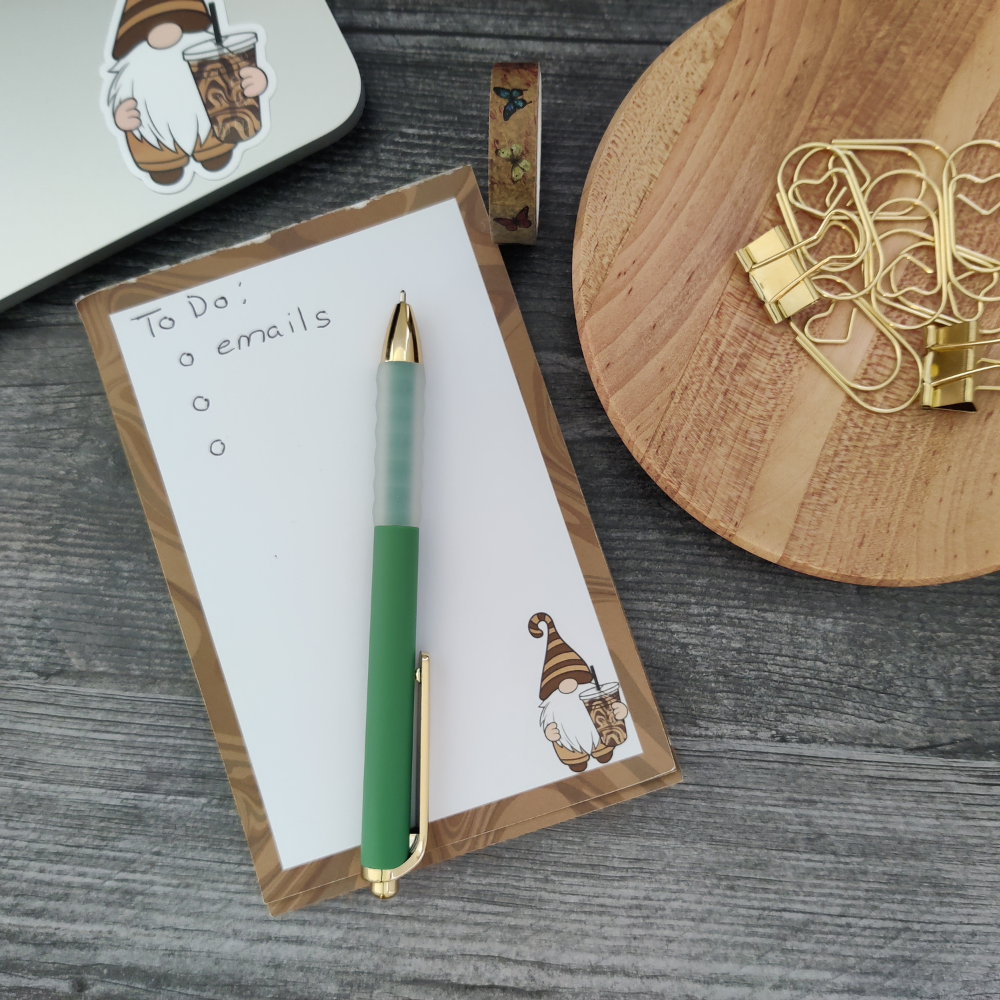 A desk with a laptop in the top left corner. Below the laptop is the brown-and-white iced coffee gnome notepad.