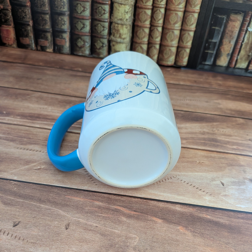 A white ceramic mug with a blue handle lying down. It shows that the bottom is white.
