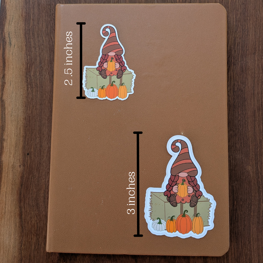Two fall pumpkin patch girl gnome stickers are sitting on a brown journal. The top sticker measures 2.5 inches wide, and the bottom sticker measures 3 inches wide.