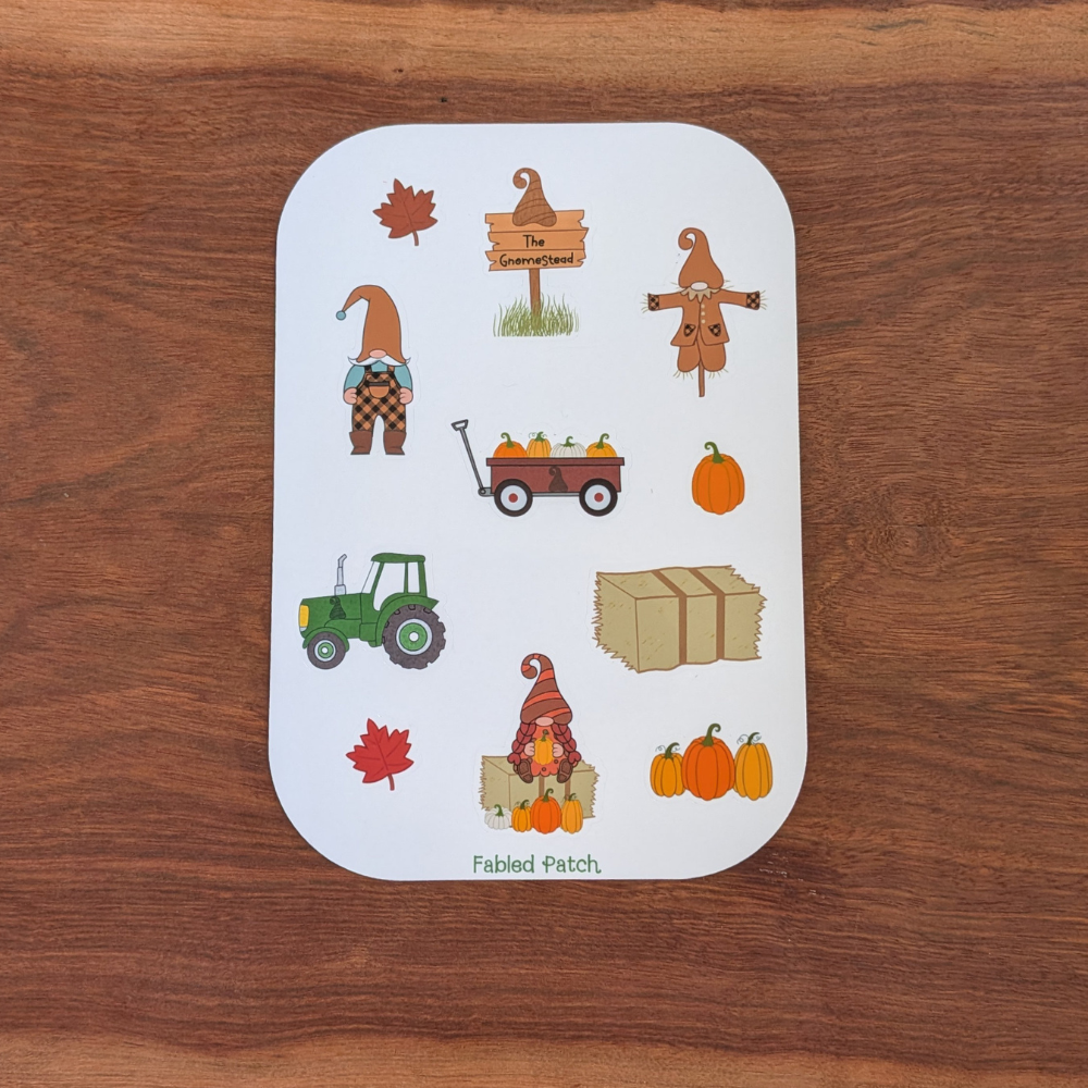 A fall gnome sticker sheet featuring 2 gnomes, a tractor, a wagon full of pumpkins, and a hay bale. The sticker sheet has brown, orange, and green colors.
