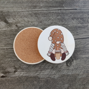 A white ceramic coaster featuring a girl gnome in a brown polka-dot dress holding an iced coffee. A back view of the coaster showing its protective cork backing.