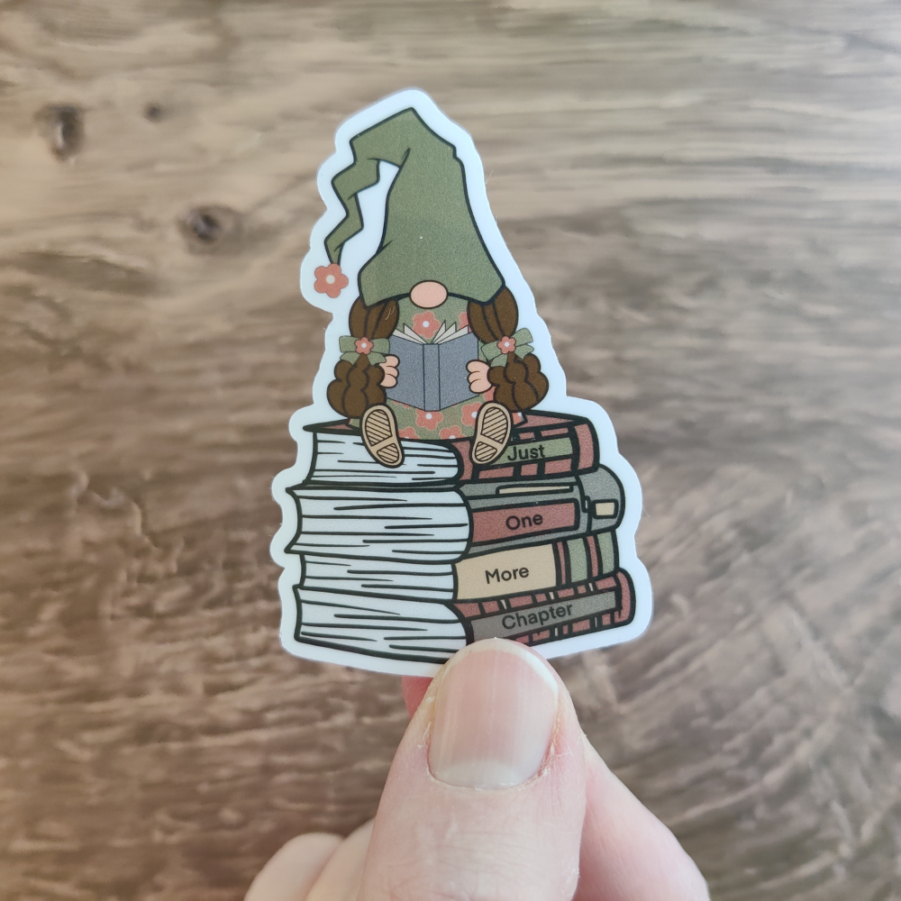 A hand is holding a girl reading a gnome die-cut sticker. The sticker has a clear laminate.
