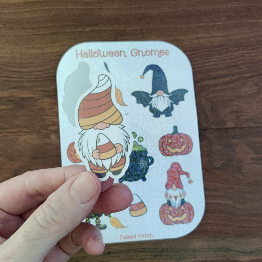 A hand holding a candy corn gnome with a sparkle laminate. The Halloween gnome sticker sheet is in the background.