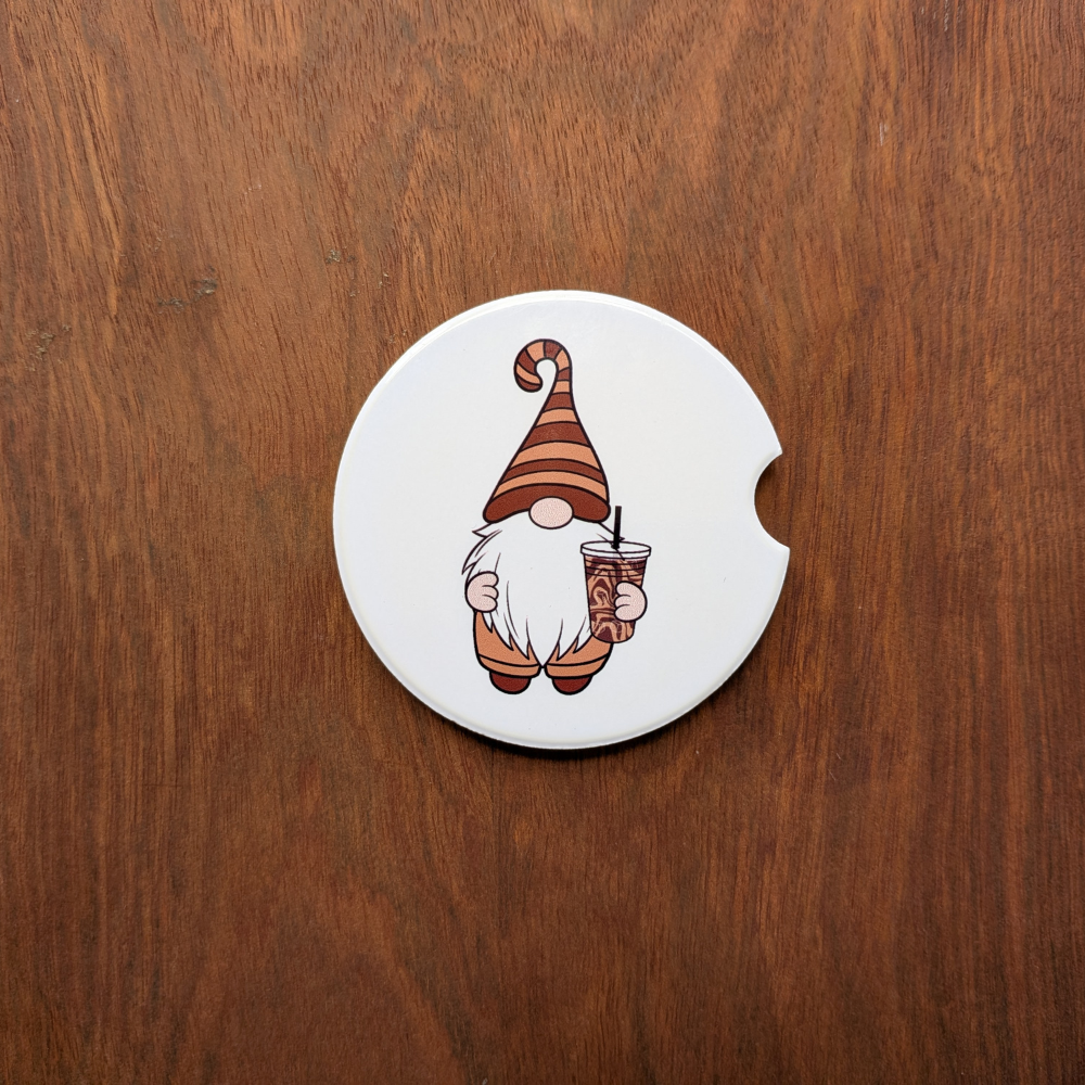 A white ceramic car coaster featuring a gnome in a brown striped hat holding an iced coffee.