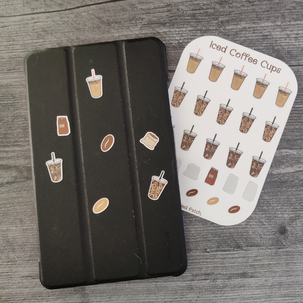 A black journal with iced coffee, coffee beans, and bag stickers. In the background is the iced coffee cup sticker sheet.