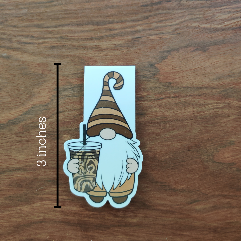 A gnome in a brown striped hat holding an iced coffee magnetic bookmark. The bookmark measures 3 inches tall when closed.