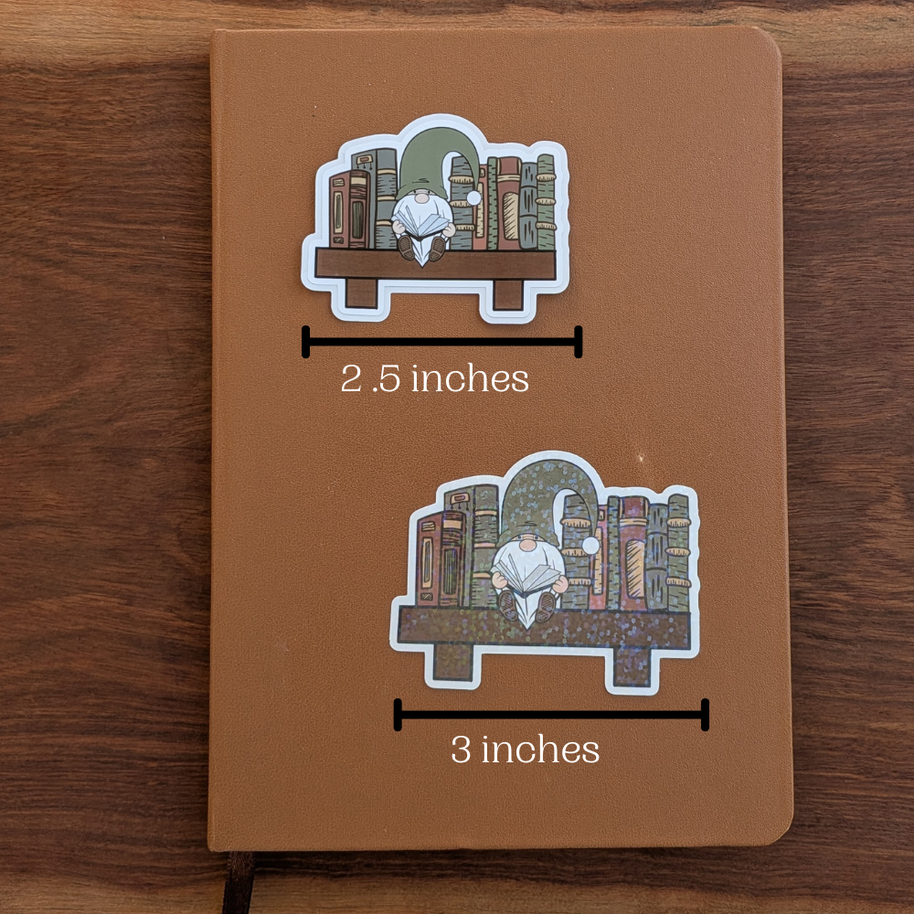 Two reading gnome stickers are sitting on a brown journal. The top sticker measures 2.5 inches wide, and the bottom sticker measures 3 inches wide.