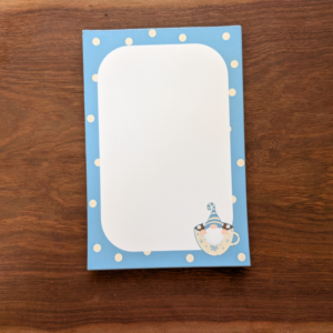 A blue and white polka-dot notepad with a winter gnome in the bottom right corner. The gnome is wearing a blue striped hat and sitting in a cup.