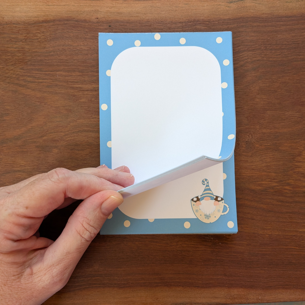 A hand flips through the winter blue and white polka-dot notepad. The winter gnome is seen on the second page in the right corner.